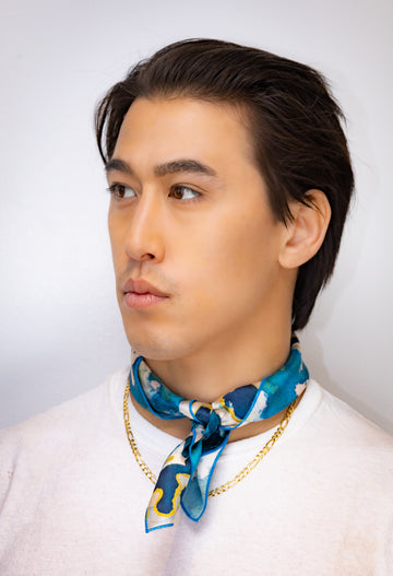 Man wearing a blue patterned scarf and gold chain necklace against a white background