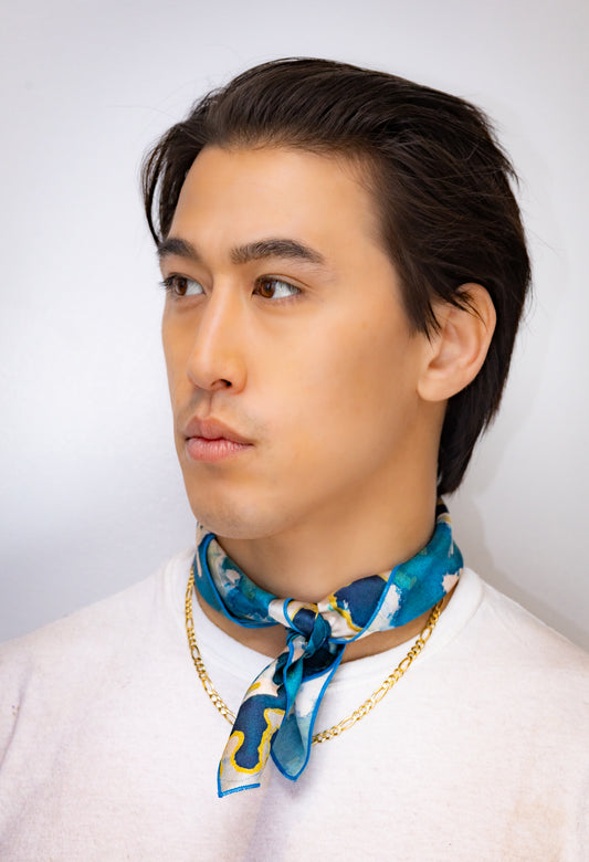 Man wearing a blue patterned scarf and gold chain necklace against a white background