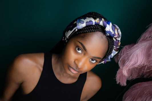 Woman with braided hair wearing a patterned headscarf against a dark background