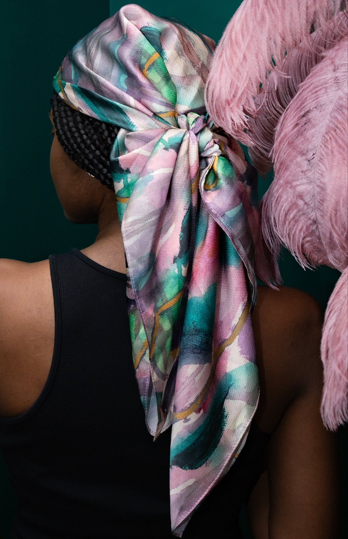 Person wearing a colorful headscarf with pink feathers against a dark background