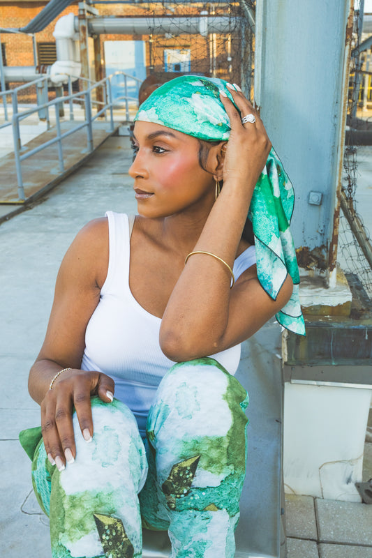 Woman sitting on a rooftop wearing green and white patterned pants and headband.