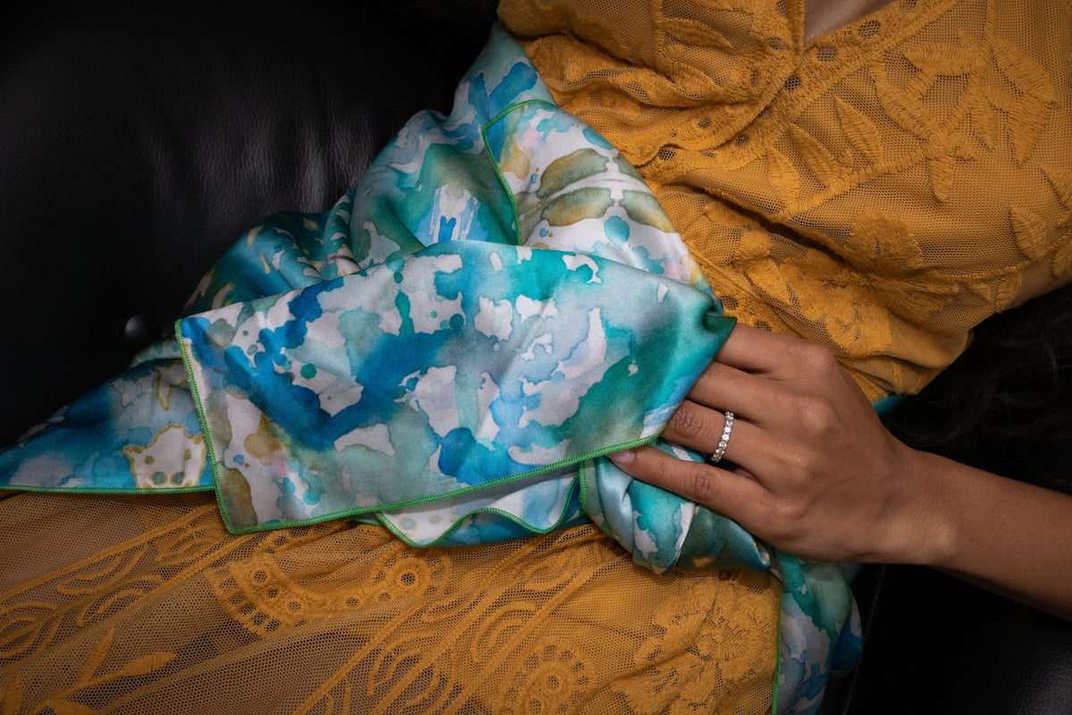 Hand holding a folded piece of fabric with blue and green floral pattern on a yellow textured surface.