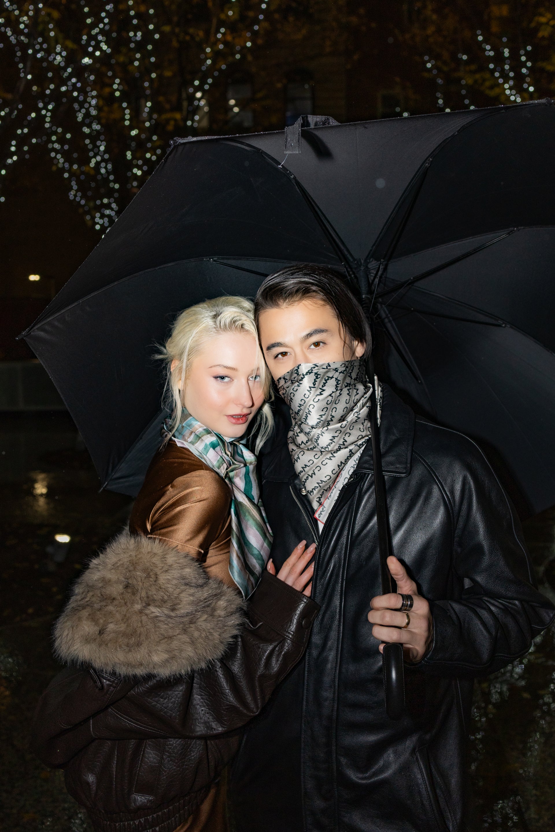 Two people hugging under a black umbrella at night.