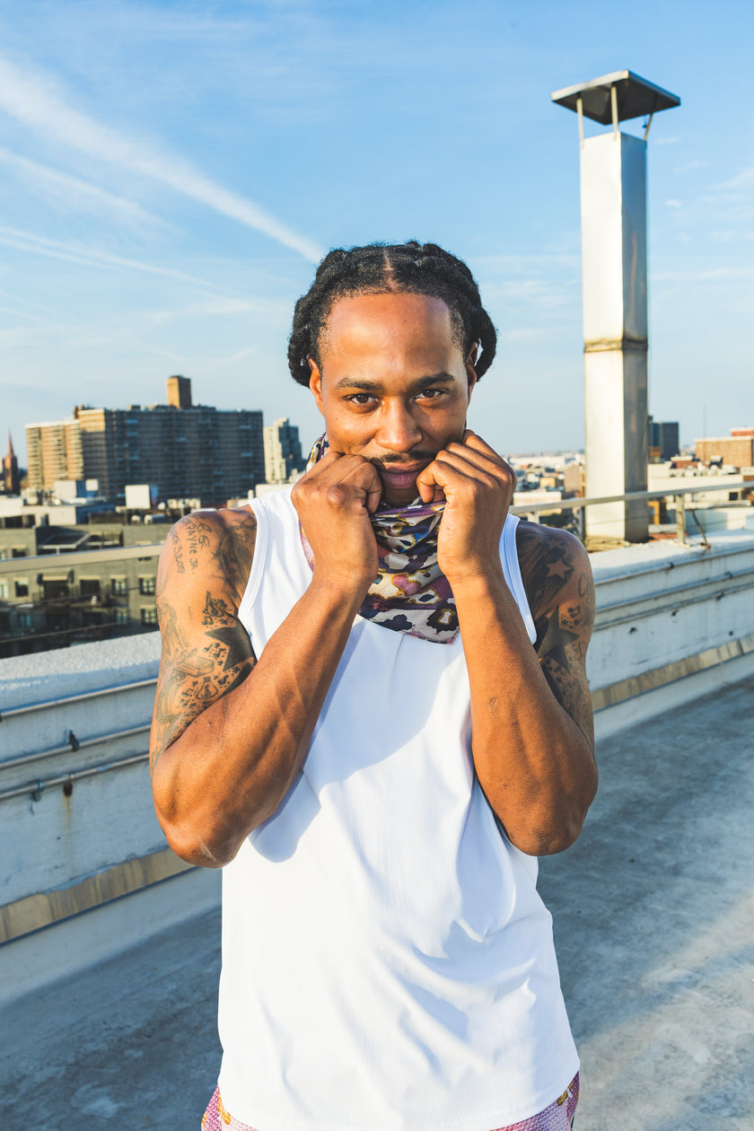 A male model poses on a rooftop wearing a white tank top with abstract-print shorts, creating a casual, confident, and stylish streetwear look.