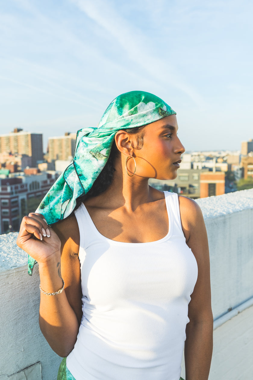 Woman wearing a green headscarf and white tank top on a rooftop