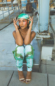 A model sits in a white tank top with green printed pants and a matching headscarf, creating a fresh, stylish, and relaxed urban fashion look.