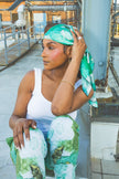 Woman sitting on a rooftop wearing green and white patterned pants and headband.