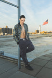 Man leaning against a railing on a rooftop with a cityscape