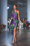 Model walking on a runway wearing a purple and green dress.