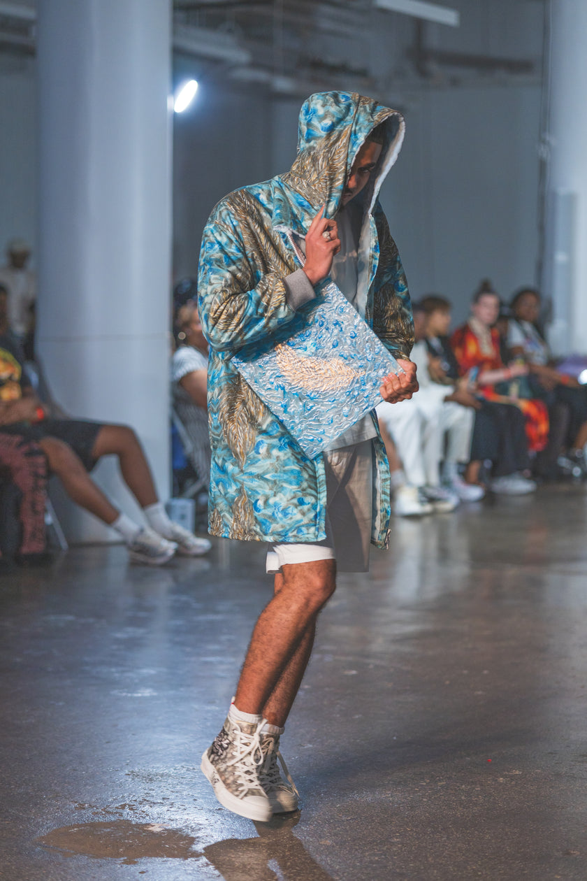 Model wearing a patterned outfit on a runway with an audience 