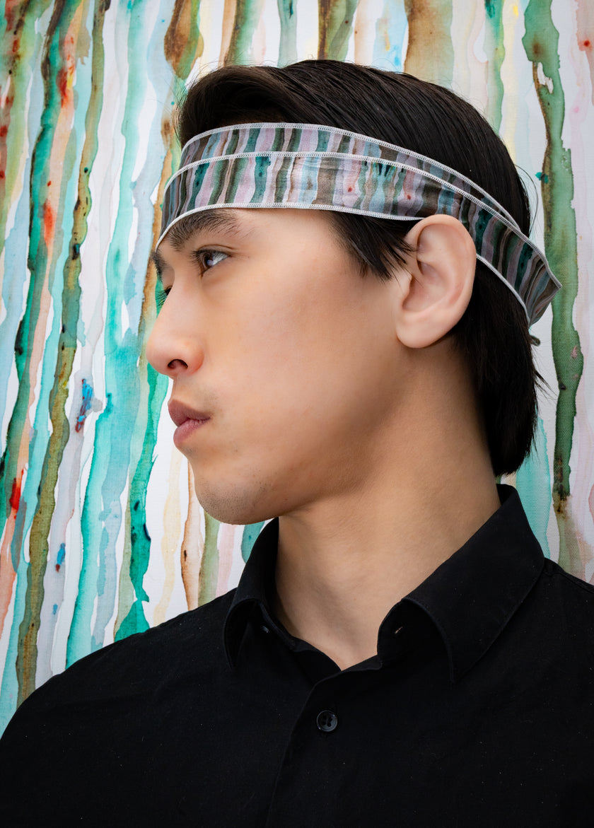 Person wearing a headband with a colorful pattern against a textured wall.