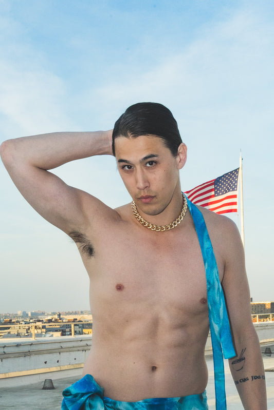 Man on a rooftop wearing a blue towel and swim shorts 