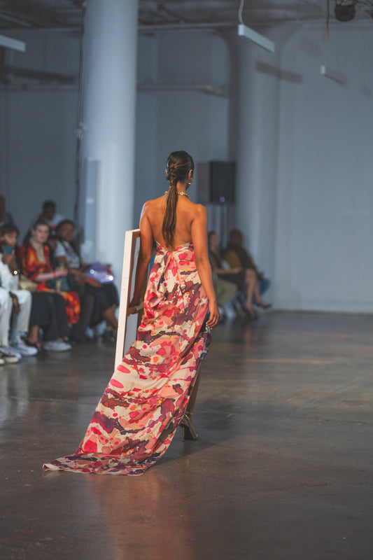 Model walking on a runway wearing a colorful dress with an audience seated