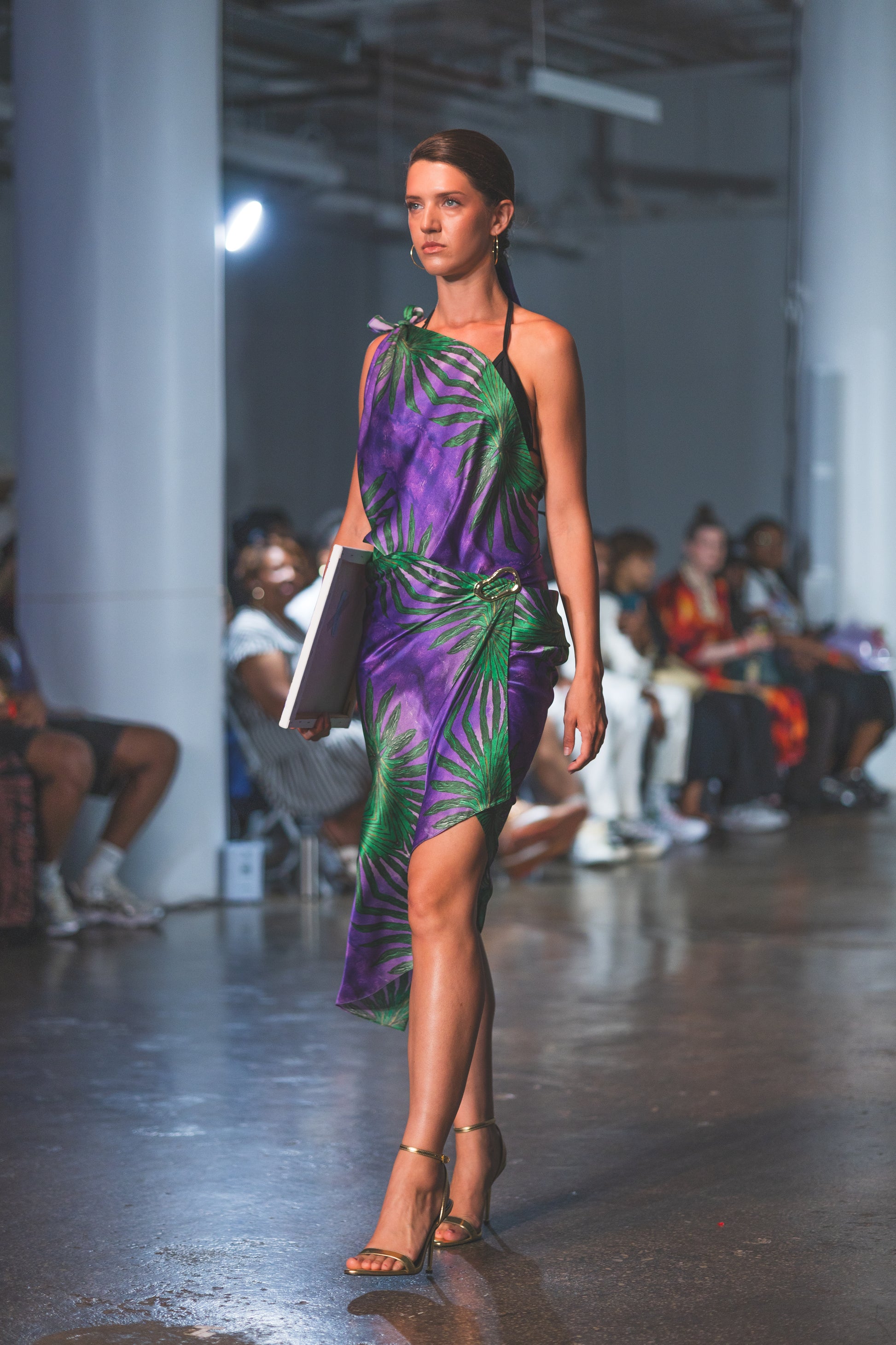 Model walking on a runway wearing a purple and green dress.