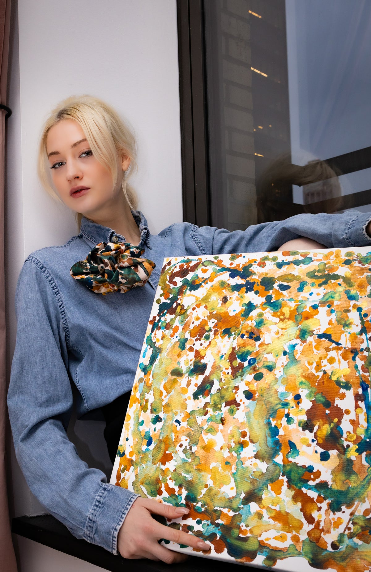Person holding a colorful abstract painting by a window