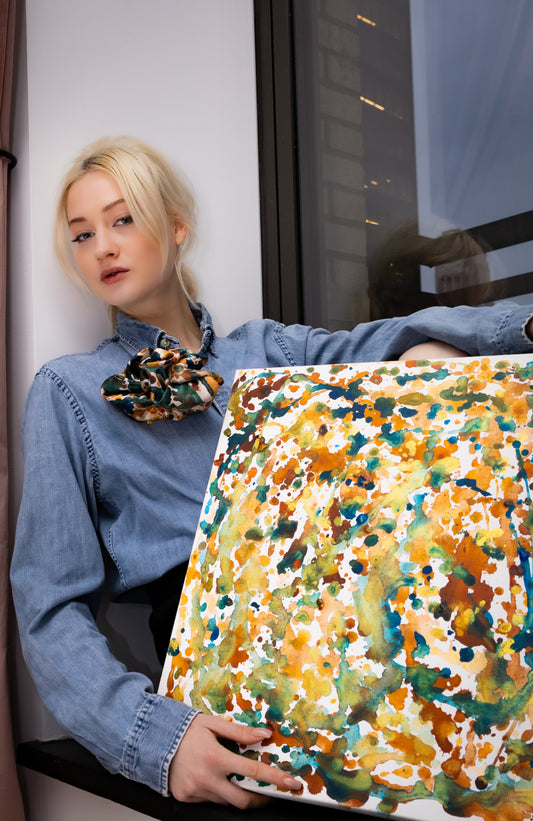Person holding a colorful abstract painting by a window