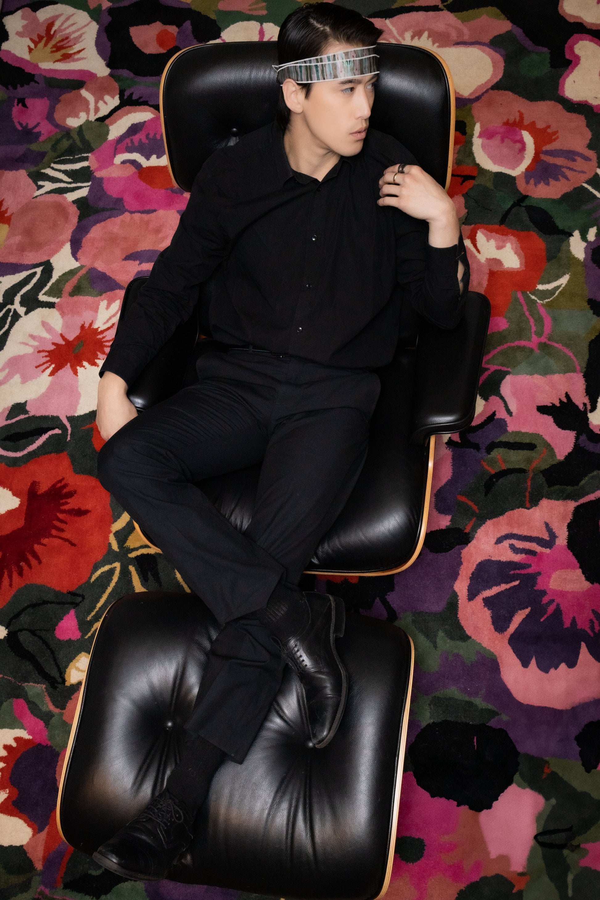 Person in black outfit sitting on a black chair with a colorful floral-patterned carpet.