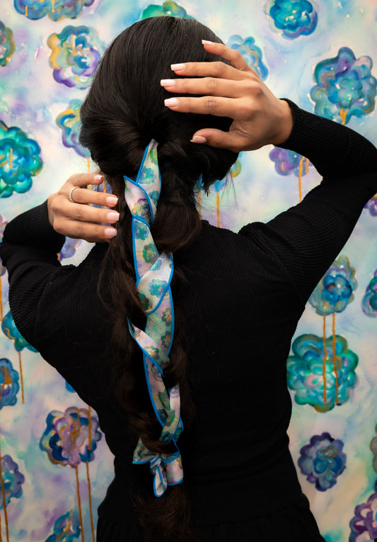 Person styling hair with a colorful scarf against a floral background