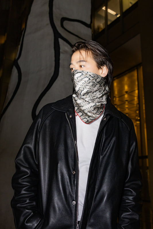 Person wearing a black jacket and patterned face mask in front of a building with large windows.