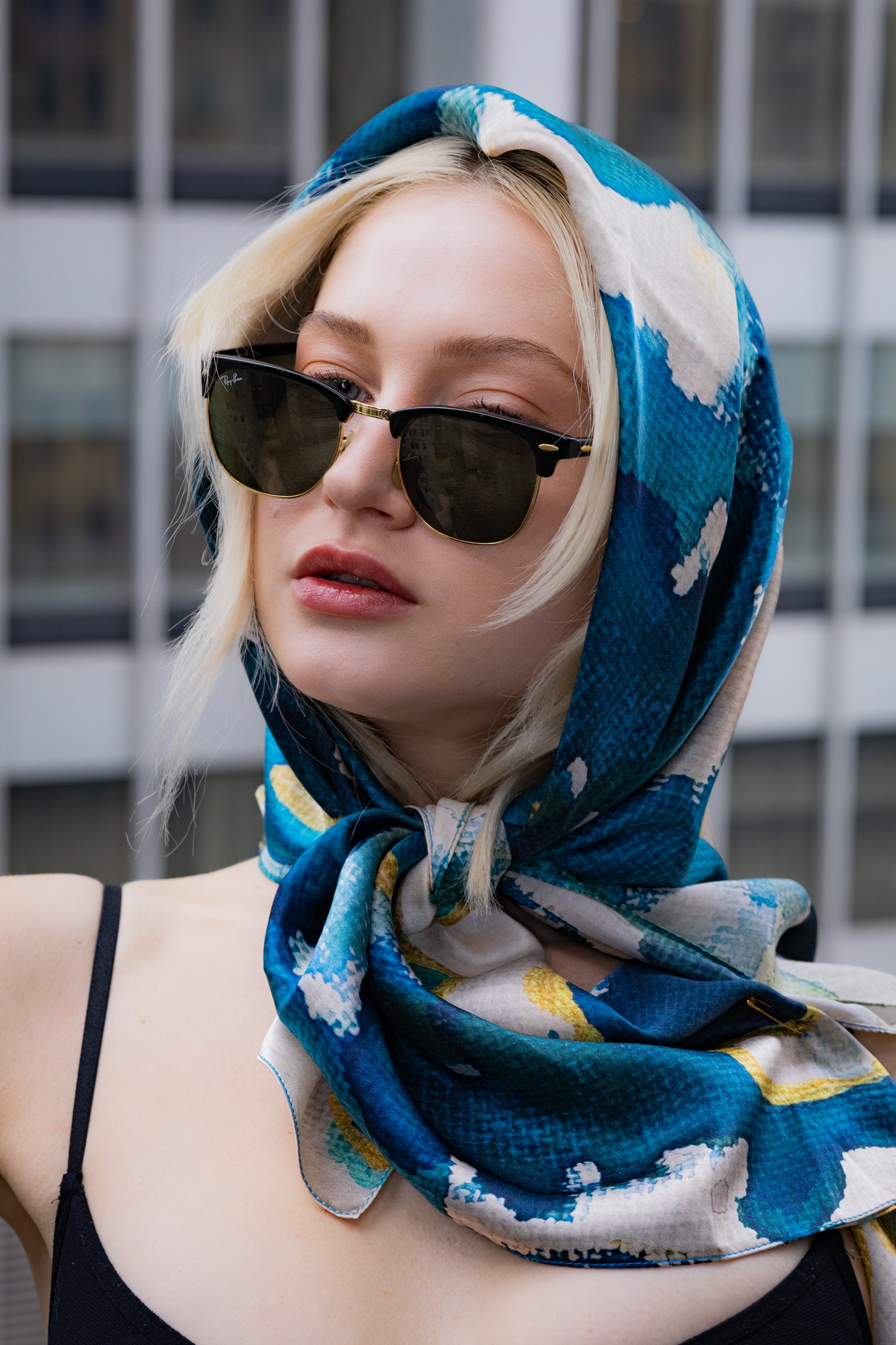 Person wearing a blue patterned headscarf and sunglasses with a blurred background