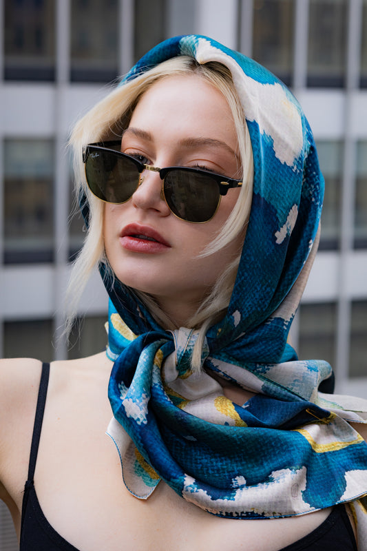 Person wearing a blue patterned headscarf and sunglasses with a blurred background