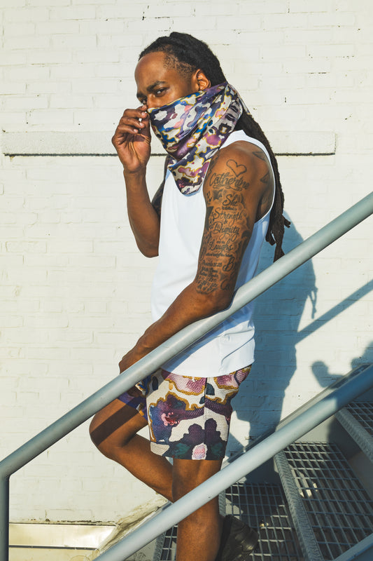 Person wearing a colorful bandana and shorts against a white wall.
