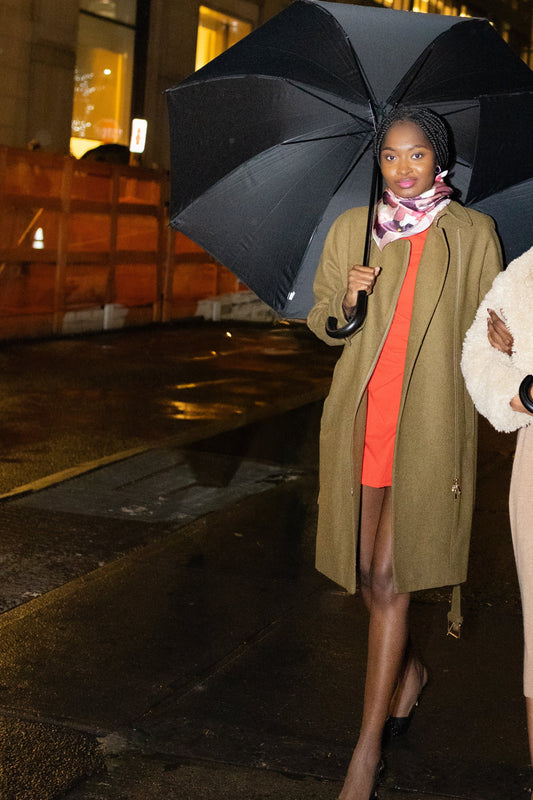 Two women walking under large black umbrellas in an urban setting at night.