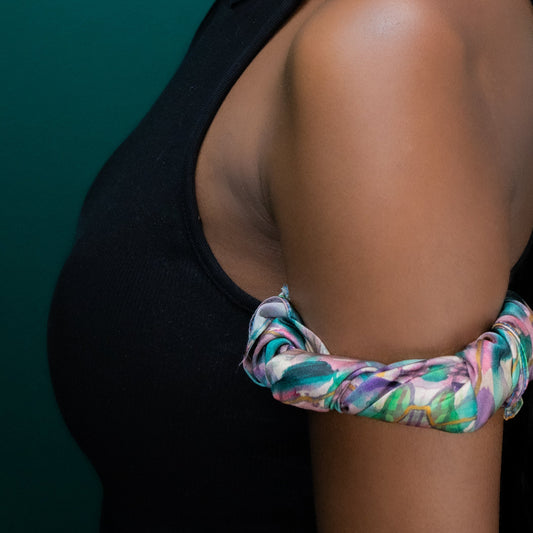 Woman wearing a colorful headscarf and matching scrunchie against a teal background
