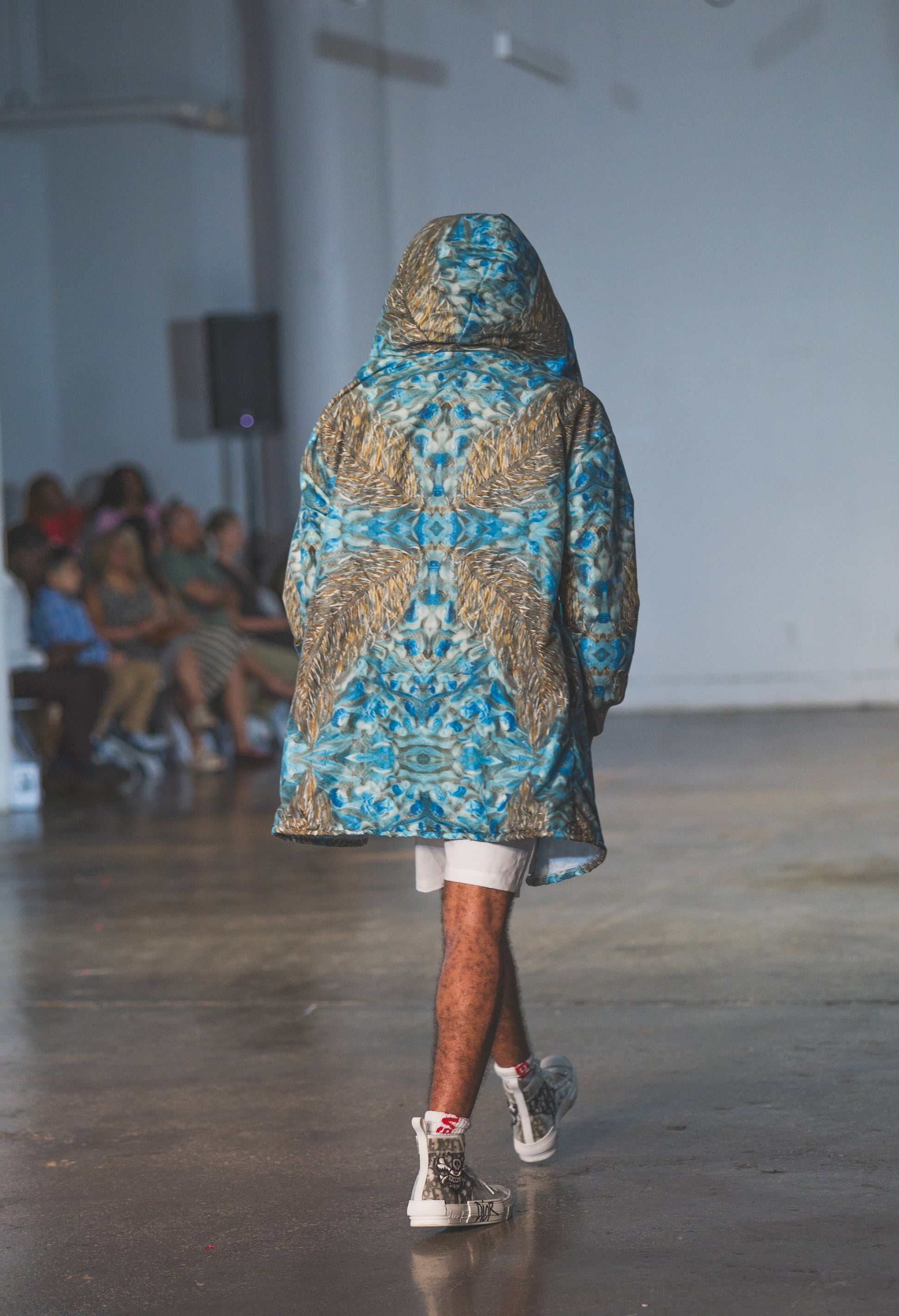Model walking on a runway wearing a patterned blue and gold jacket.