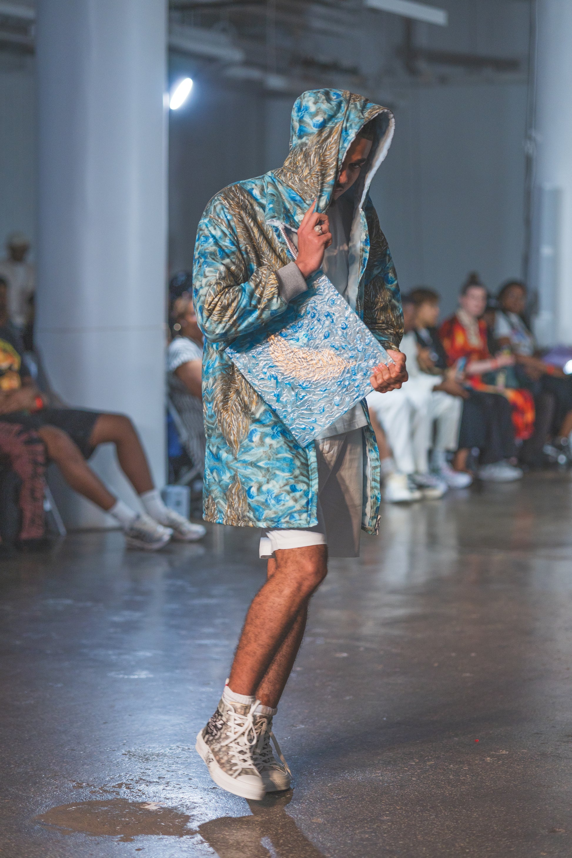 Model wearing a patterned outfit on a runway with an audience 
