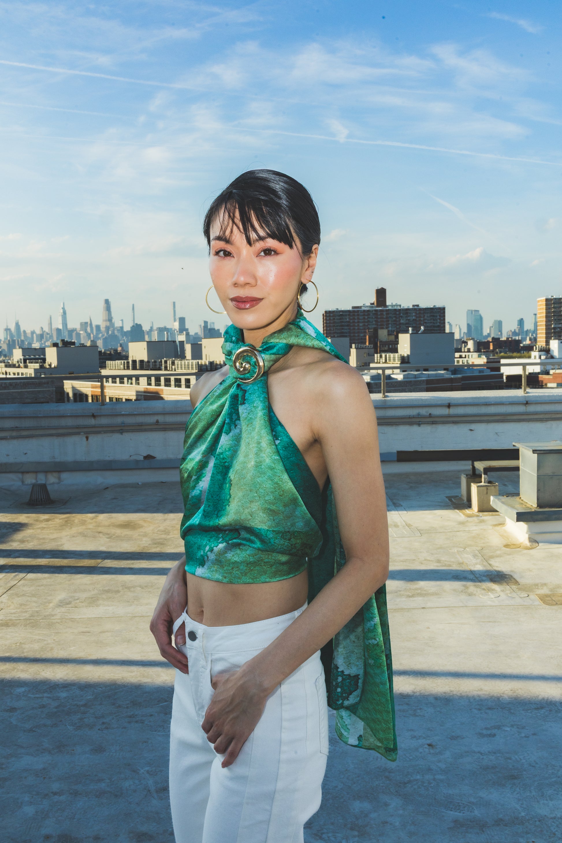Woman in a green top and white pants standing on a rooftop 