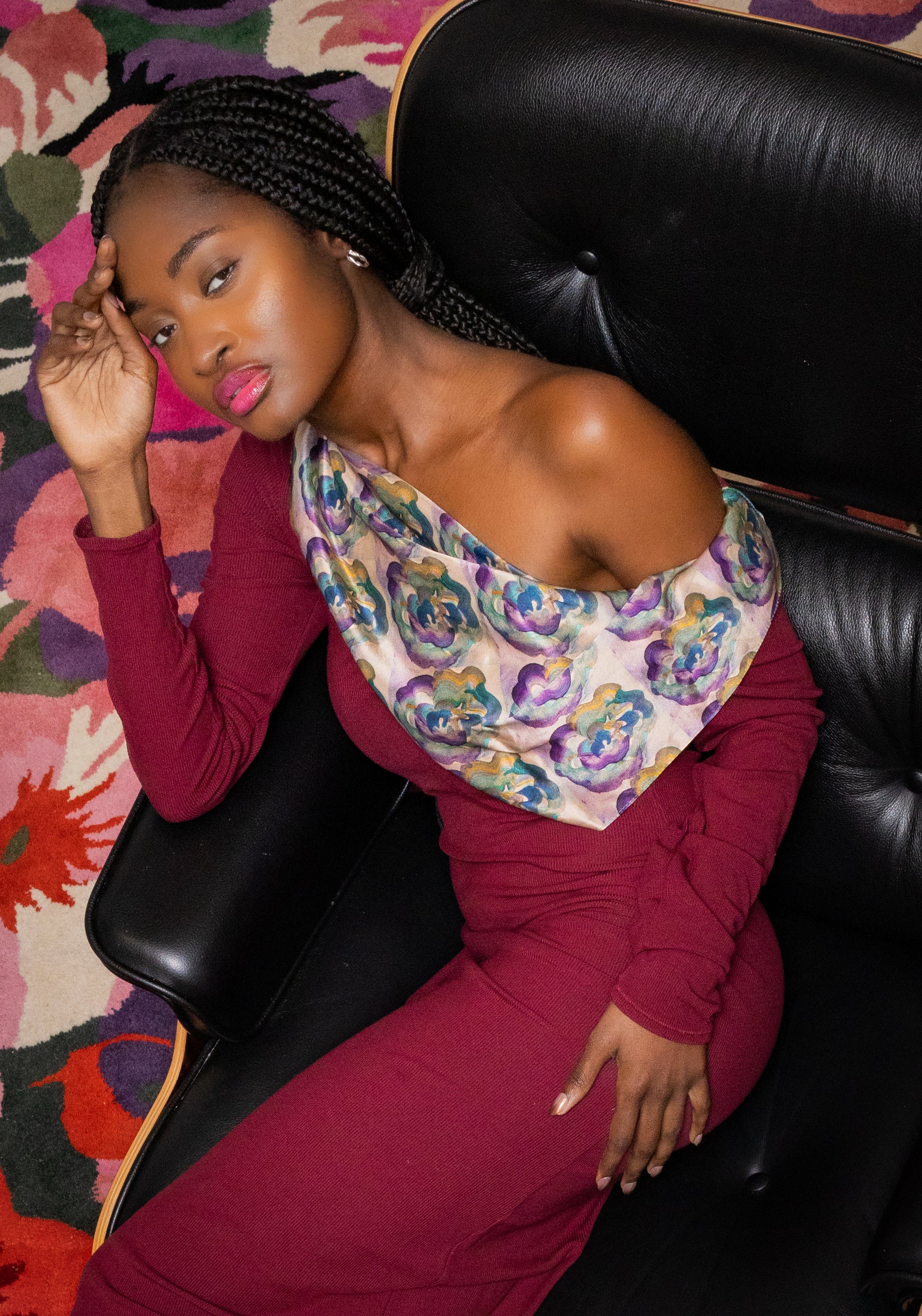 Woman sitting on a black leather chair wearing a colorful scarf and red outfit.