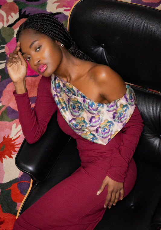 Woman sitting on a black leather chair wearing a colorful scarf and red outfit.