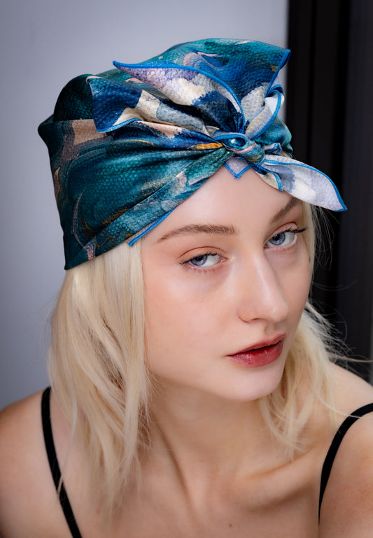 Woman wearing a blue and green patterned headscarf against a neutral background