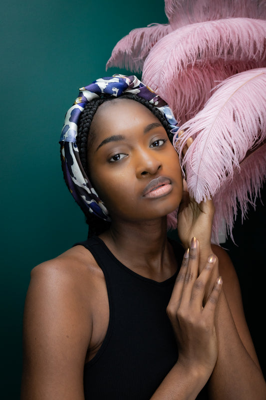 Woman wearing a colorful headscarf with pink feathers against a dark background