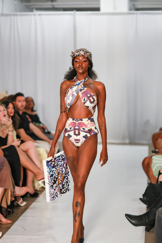 Model wearing the Andromeda Cuore swimsuit with a cross-over halter neckline and open front on a runway.