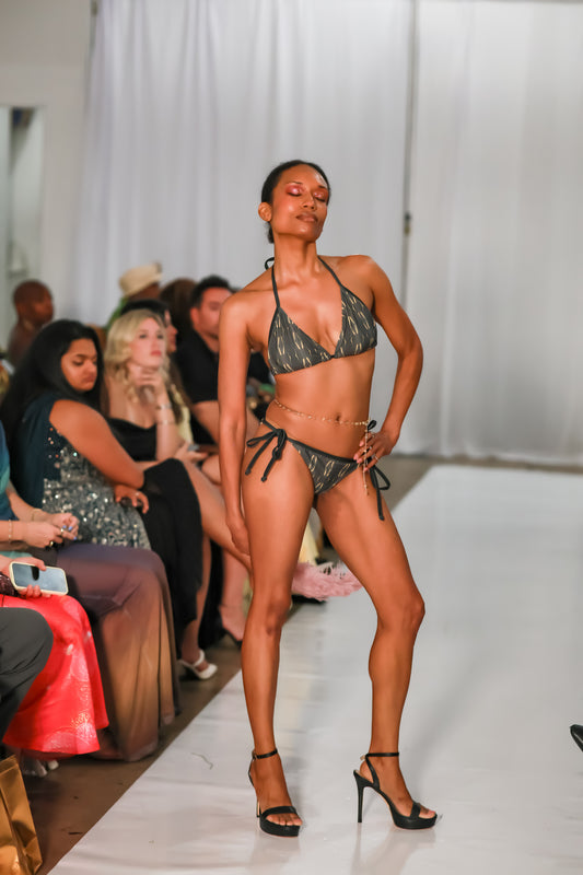 Model posing on a white runway in cheeky swimsuit bottoms with adjustable ties and a minimal coverage fit, by C. Monet Atelier