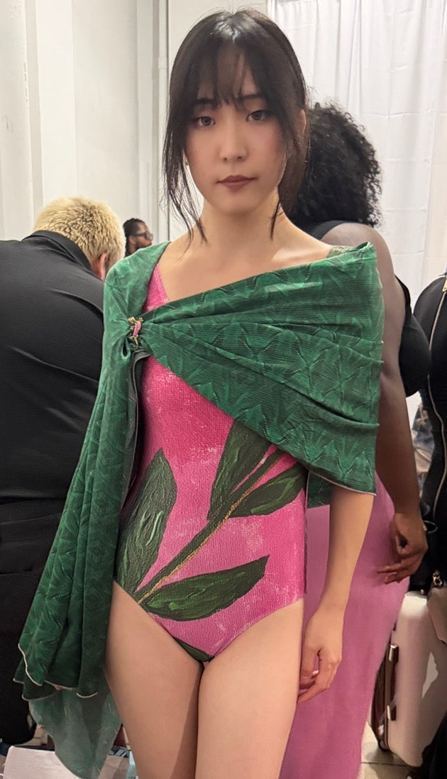 Close-up of a floral one piece swimsuit in pink with a bold green leaf design, worn with a green silk scarf on the shoulders