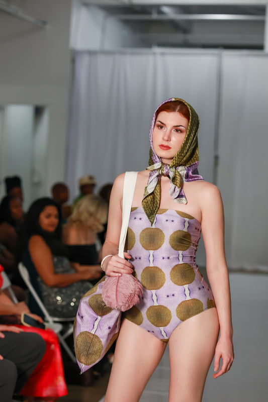 Model wearing a lavender one piece swimsuit with gold coin print on runway