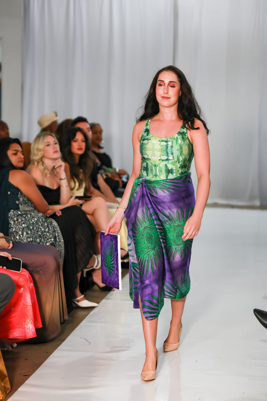 Full-length front view of a women's green one piece swimsuit worn with a purple wrap skirt on the C. Monet runway