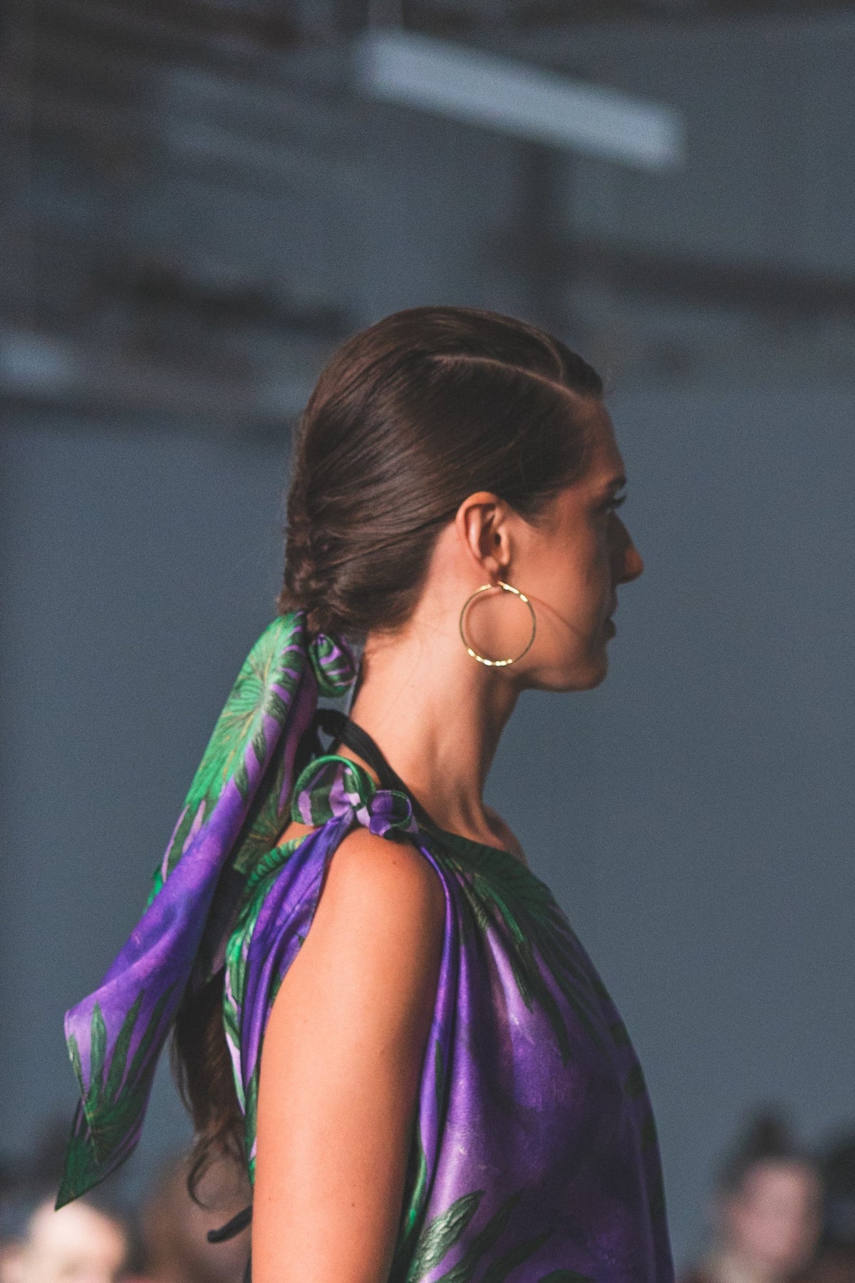 Side view of a model with a purple and green silk scarf tied around her ponytail.