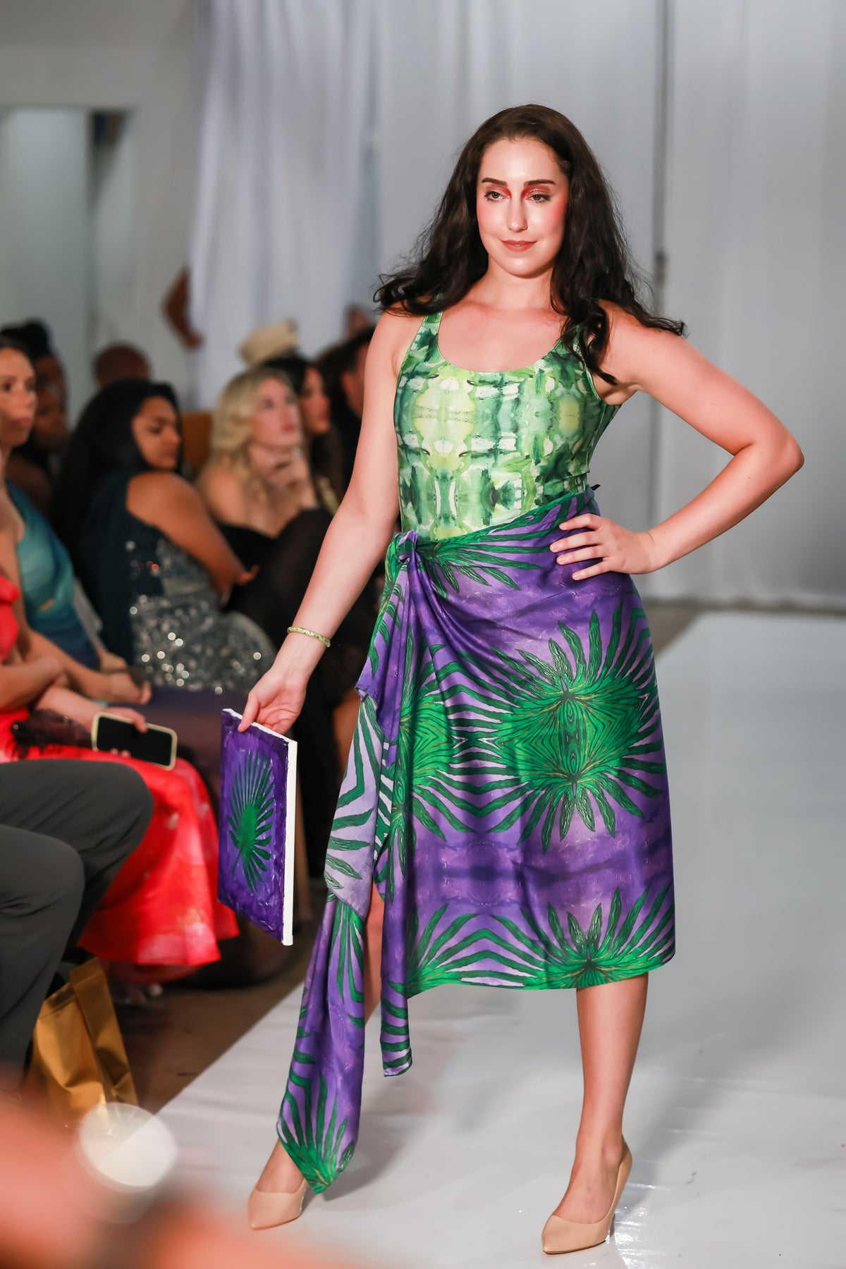Runway model wearing a purple and green scarf around her waist with a green printed top.