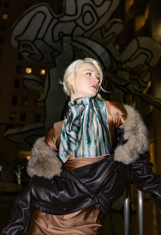 Person wearing a stylish outfit with fur-trimmed jacket and patterned scarf in an urban setting.